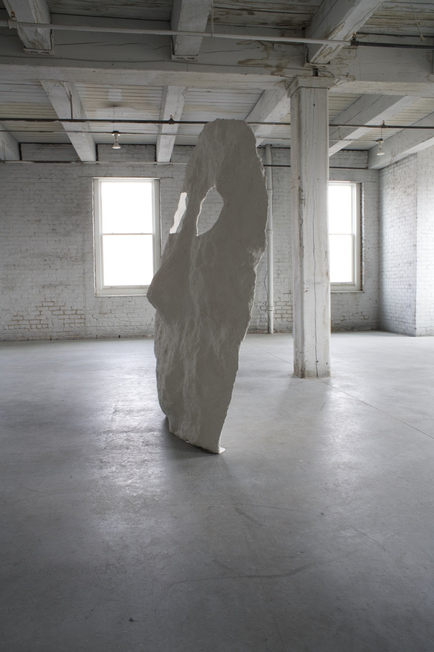 Photograph of large white sculpture reminiscent of face in a warehouse