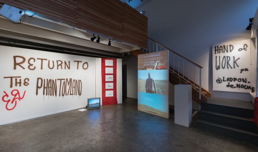 Photo of installation including graffiti-like words on walls, a projected video on a screen