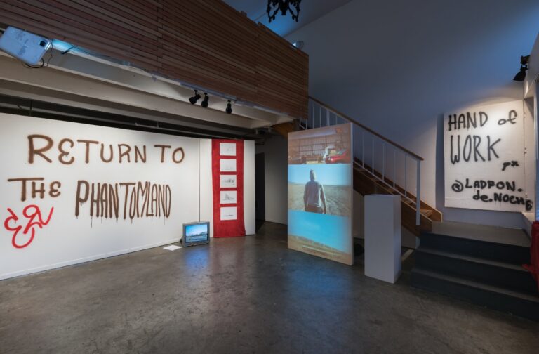 Photo of installation including graffiti-like words on walls, a projected video on a screen