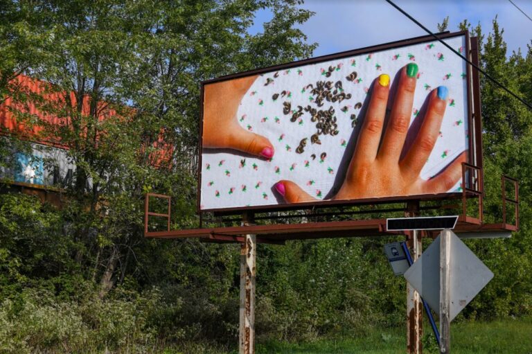 Photo of a billboard with tress in the background. Billboard shows photo of child's hands and seeds.